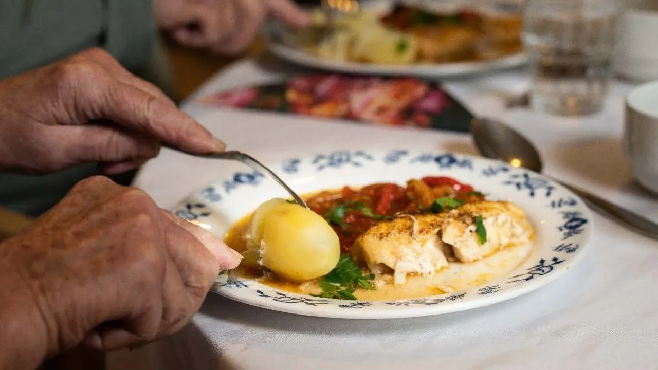 En person som skjærer et stykke mat på en tallerken.