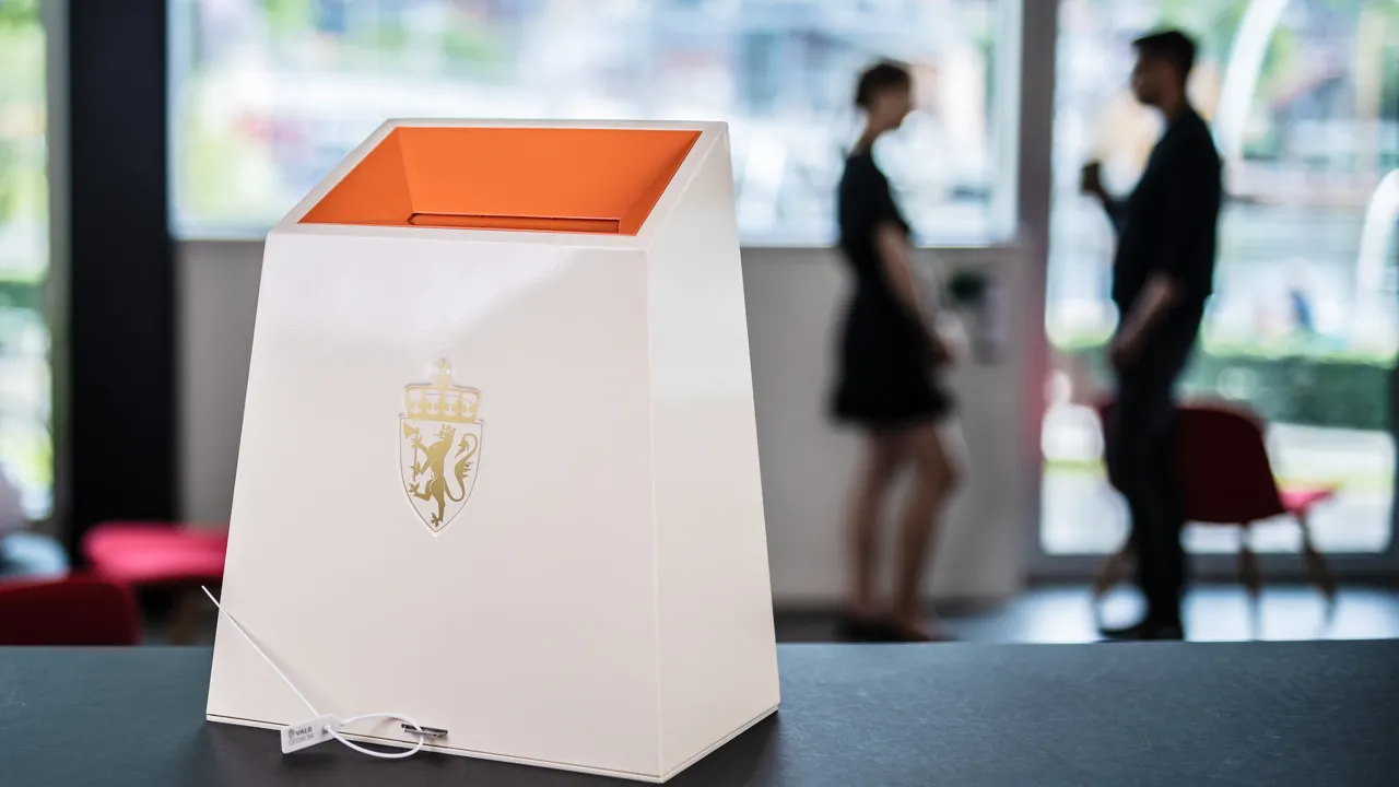 En oransje og hvit valgurne som står på toppen av et bord.