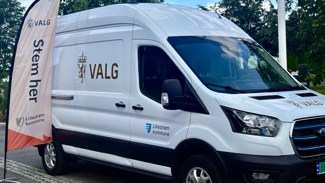 En hvit varebil står parkert ved siden av et flagg.