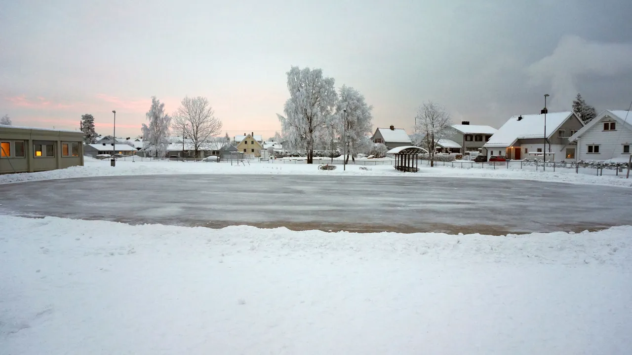 Et snødekt isbane med hus i bakgrunnen.