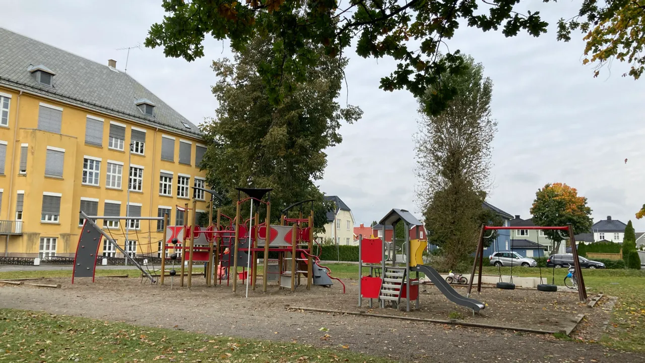 En lekeplass foran en stor gul bygning.